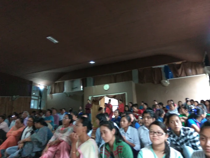 A packed auditorium audience of students and residents during a programme.
