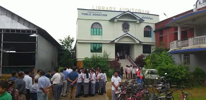 A crowd of students and visitors gathered outside the auditorium, with bicycles parked alongside.